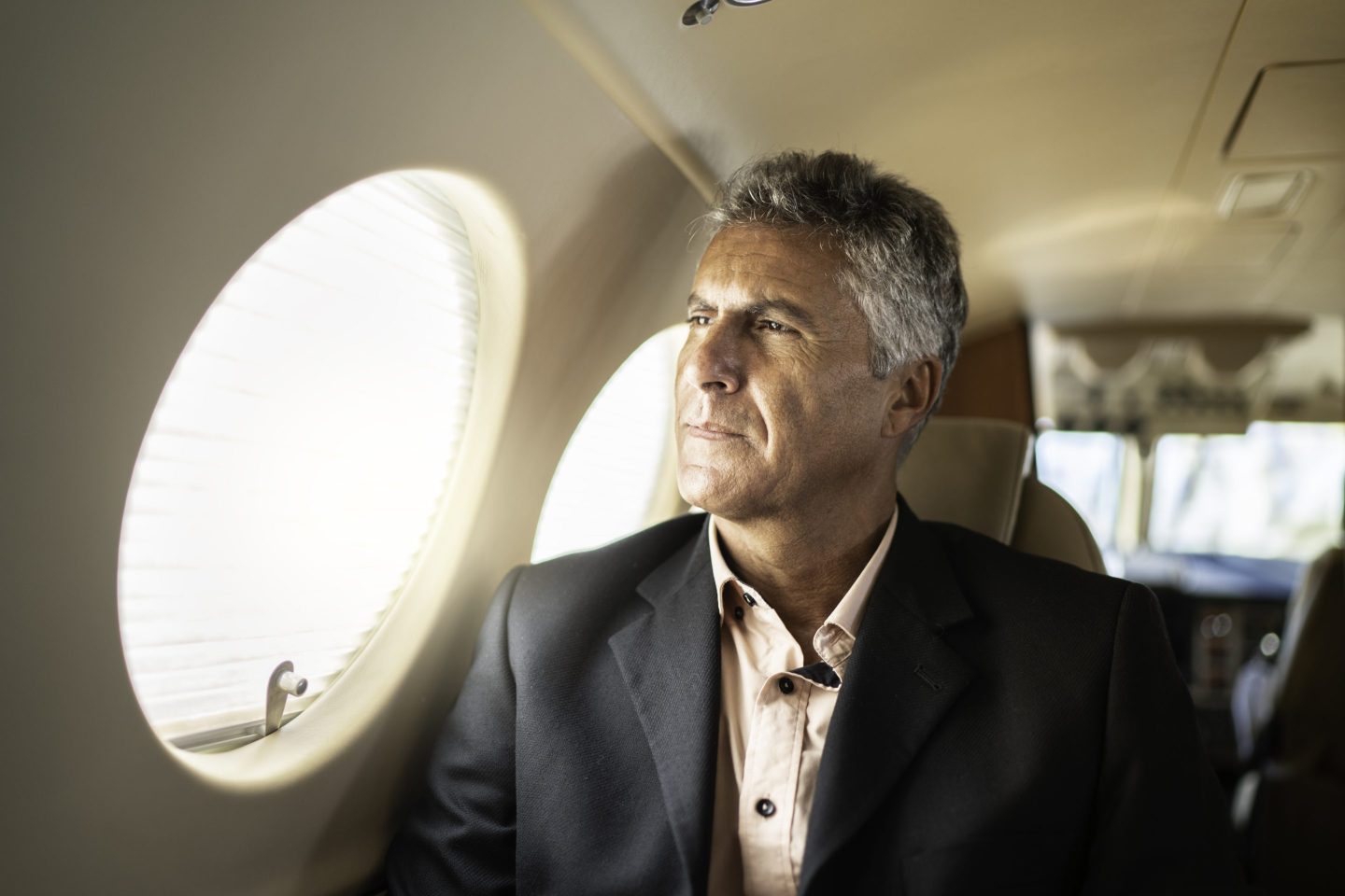 Mature man businessman looking through corporate jet window