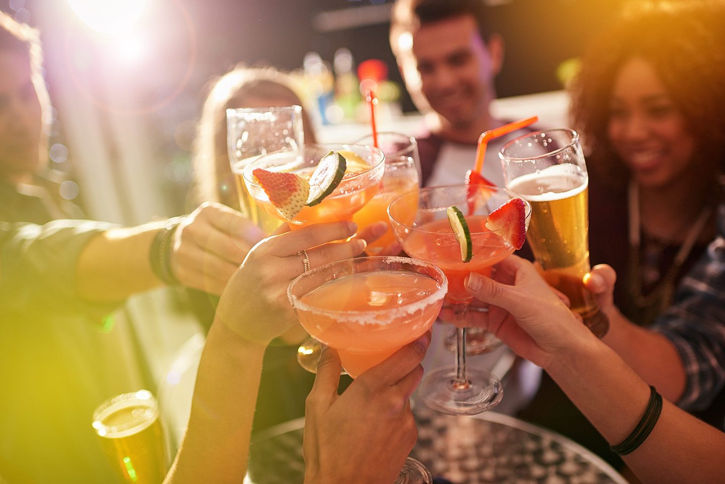 Closeup of various cocktails with people in background toasting each other